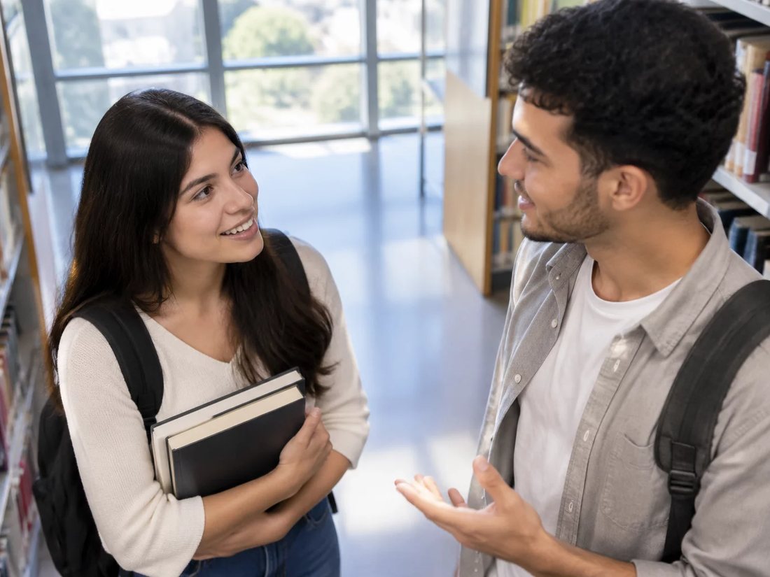 Conversa em pé entre as estantes da escola, com folhas de anotação na mão de quem discute